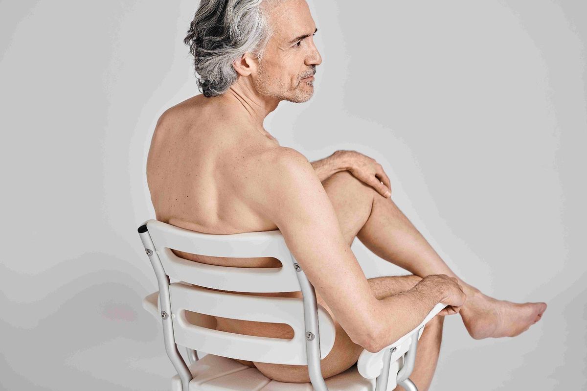 A man seated on the white Bue Shower Chair, seen from behind
